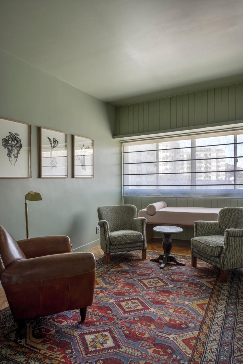 Sala de consulta de paredes verde-claras, com quadros, poltronas e tapete, no consultório da Dra. Mariana Fonseca